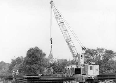 171739 Afbeelding van het laden van een spoorstaaf met behulp van een kraan op de stapelplaats van de N.S. te Crailoo.